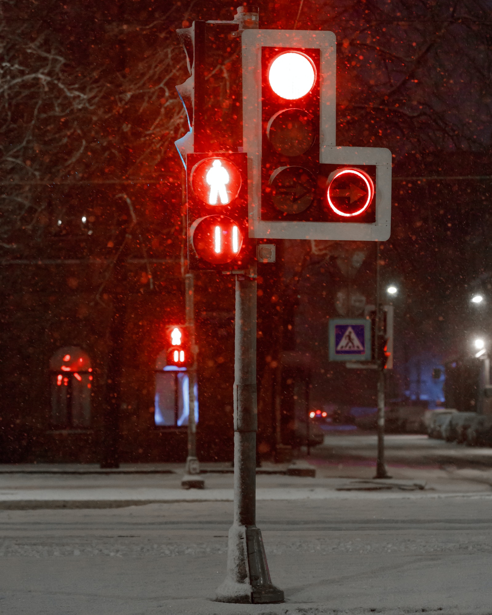 Traffic lights with red for transport and pedestrians during a snowfall at night